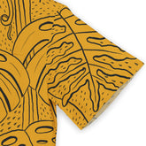 Close-up of a mustard yellow shirt sleeve with black abstract leaf patterns, featuring curved lines and dotted details.