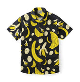 A black short-sleeve shirt featuring a playful banana print with whole bananas, banana slices, and peeled bananas in bright yellow and cream tones.