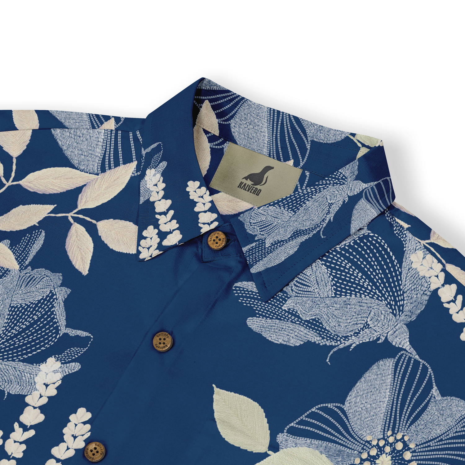 This close-up view showcases the intricate floral pattern of the shirt, highlighting the detailed stitching and the contrast between the soft leaves and the rich blue background. The delicate button details add a refined touch, making it a versatile piece for both casual and semi-formal summer outings.