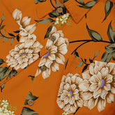 Close-up of a shirt with a floral design, featuring large beige and white flowers with green leaves on an orange background. The details highlight the intricate petals and delicate button accents, creating a bold yet elegant look.