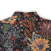 A close-up of a fabric design with a vibrant mix of flowers and leaves in colors like orange, red, yellow, green, and white on a dark background.