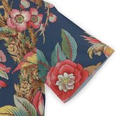 Close-up of a shirt sleeve featuring a colorful floral and leaf design on a dark blue background, with shades of red, pink, green, and yellow.