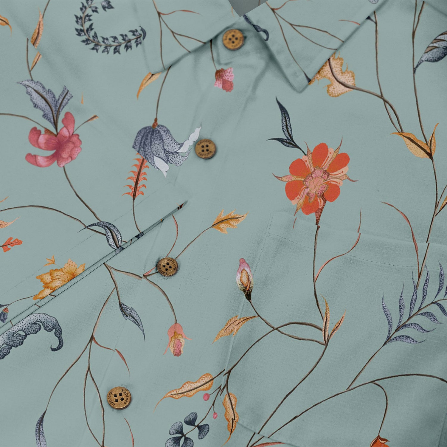 Close-up of a light green shirt with a detailed floral and botanical design, featuring colorful flowers, thin branches, and natural elements, complemented by wooden buttons.